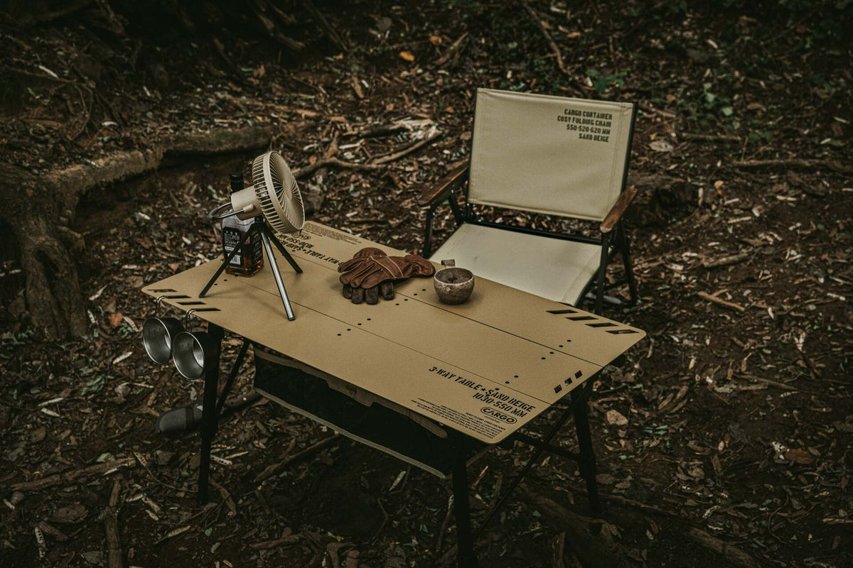CARGO CONTAINER table, camping chair and portable fan at a woodland campsite