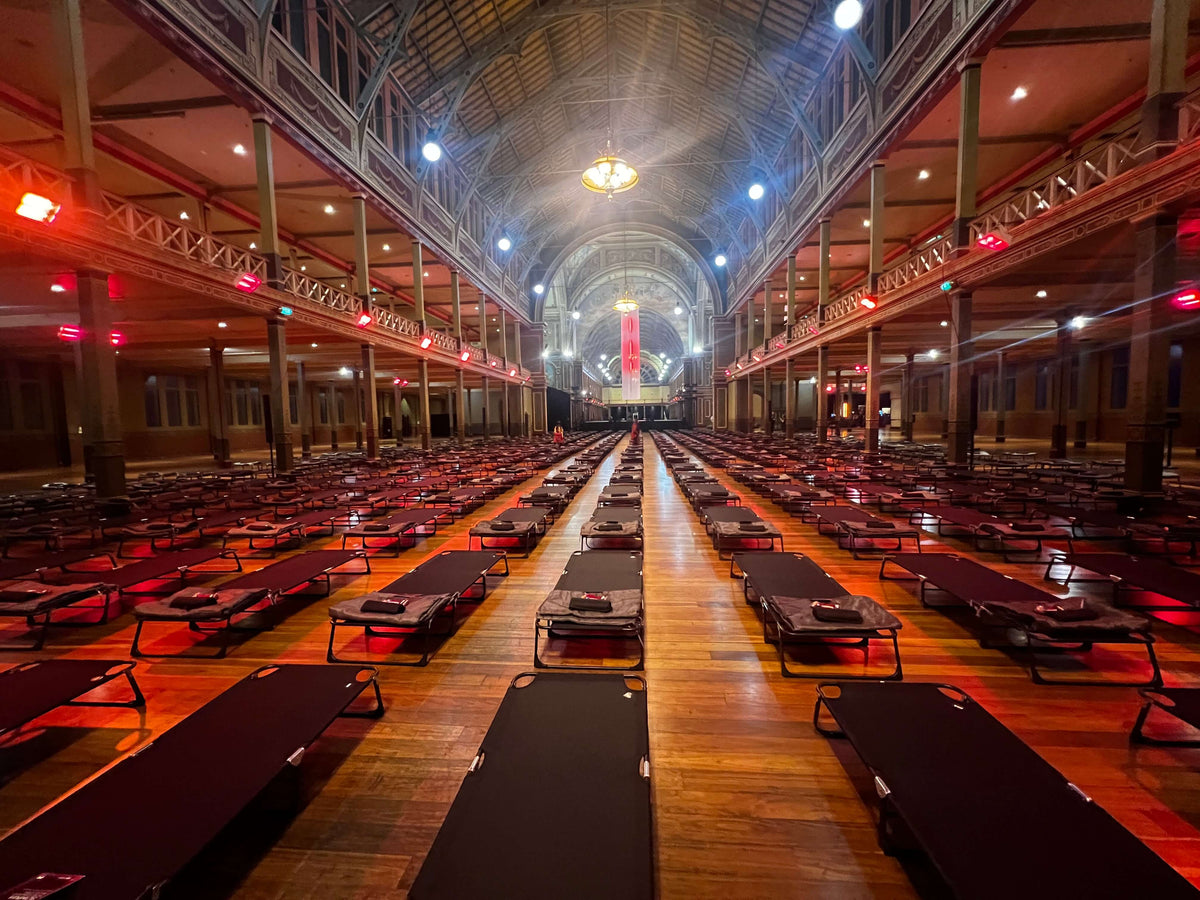 Rows of camp stretchers inside Melbourne’s Royal Exhibition Building for Now or Never, supported by Cosy Camp.