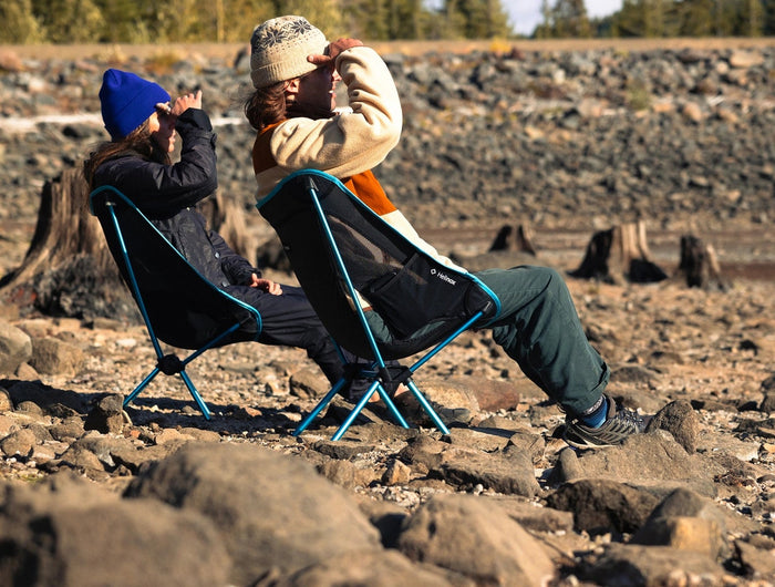 Camper seated in a Helinox Chair One (re) on a rocky lakeshore.
