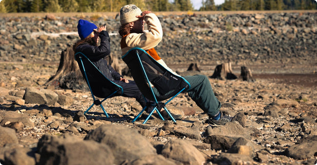 Camper seated in a Helinox Chair One (re) on a rocky lakeshore.