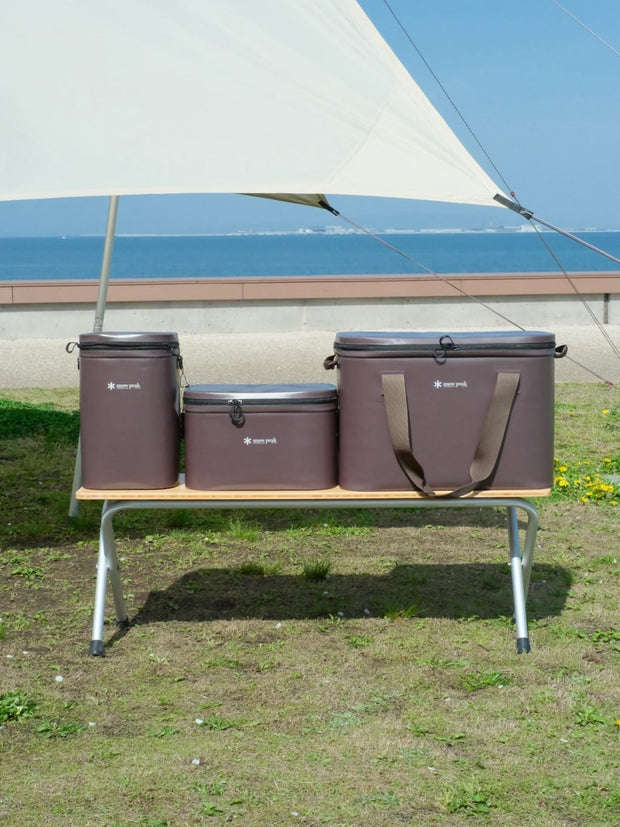 SNOW PEAK Soft Coolers on a camping bench under a tarp beside the sea